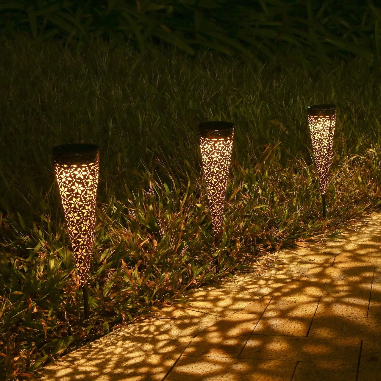 Solarleuchten im Garten bei Nacht, die einen beleuchteten Weg entlang eines Rasens zeigen. Diese Solarleuchten sind ideal für die Wegbeleuchtung und bieten eine energieeffiziente und umweltfreundliche Lösung. Erhältlich bei OBI, Aldi 2022 und Lidl.